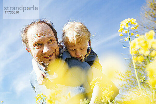 Glücklicher Vater mit Tochter am Rapsfeld an einem sonnigen Tag