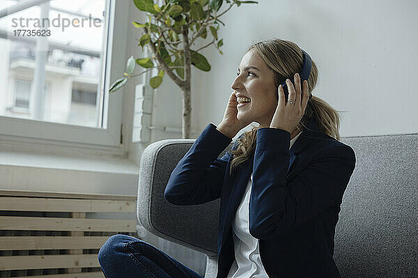 Glückliche Geschäftsfrau  die im Büro Musik über kabellose Kopfhörer hört