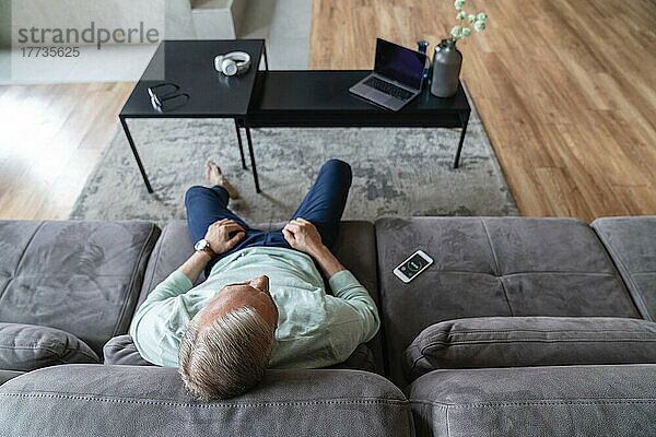 Mann mit Timer auf Mobiltelefon entspannt sich im heimischen Wohnzimmer