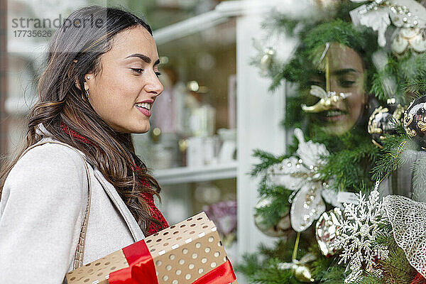 Lächelnde Frau mit Weihnachtsgeschenk beim Schaufensterbummel