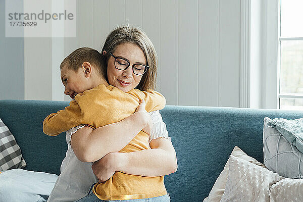 Glückliche Frau umarmt Sohn  der zu Hause auf dem Sofa sitzt