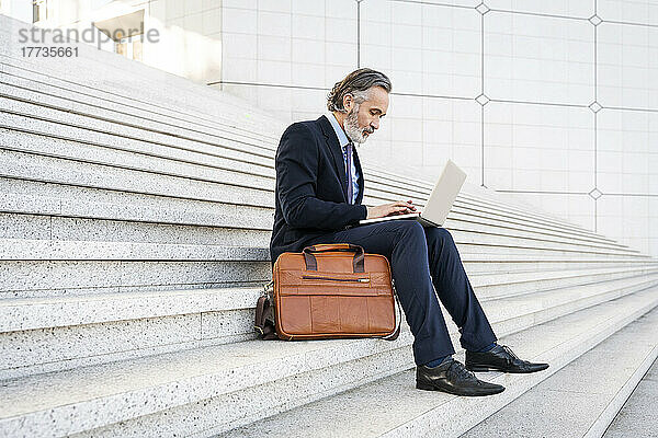 Reifer Geschäftsmann mit Laptop auf Stufen sitzend