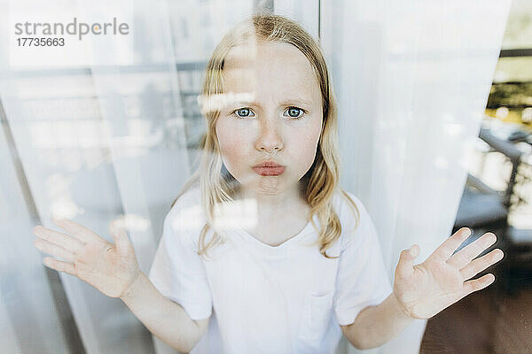 Besorgtes Mädchen steht zu Hause am Glasfenster