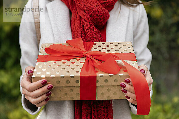 Junge Frau hält Weihnachtsgeschenk mit roter Schleife