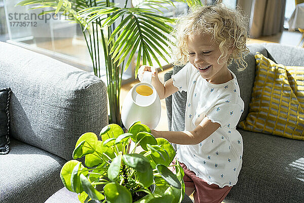 Smiling girl with blond hair watering plant at home