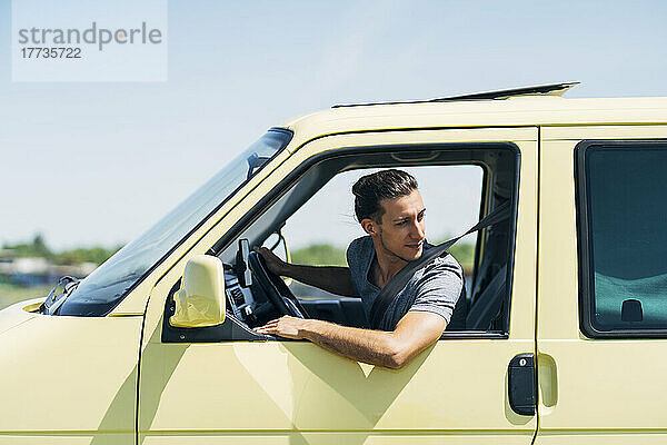 Young man looking out of van's window on sunny day