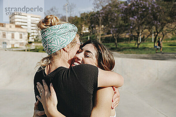 Happy woman embracing friend at skateboard park on sunny day