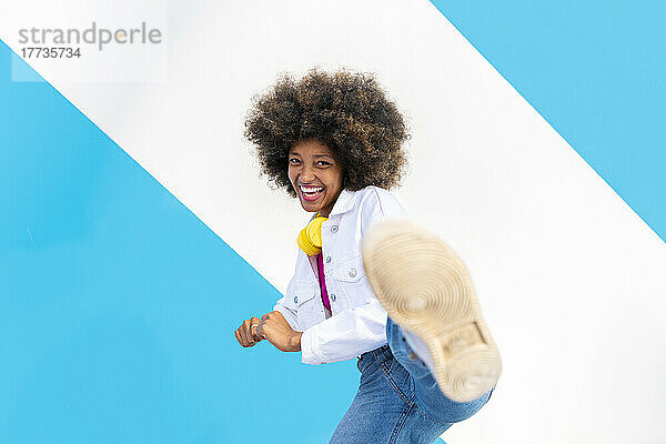 Glückliche junge Afro-Frau tritt vor einer blau-weißen Wand