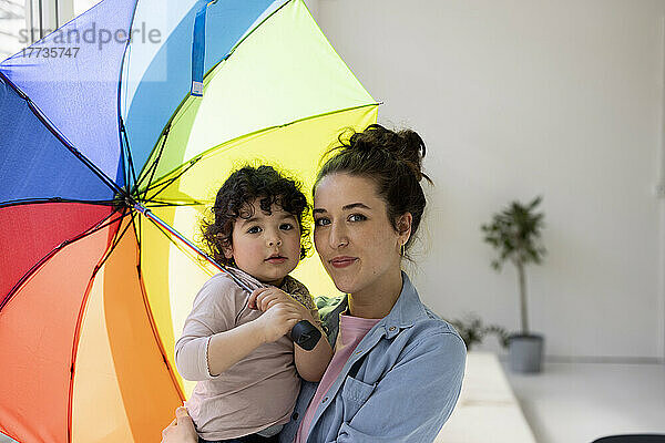 Mutter und Tochter stehen zu Hause und halten einen Regenschirm