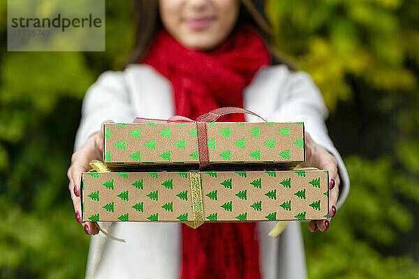 Junge Frau in warmer Kleidung überreicht Weihnachtsgeschenke