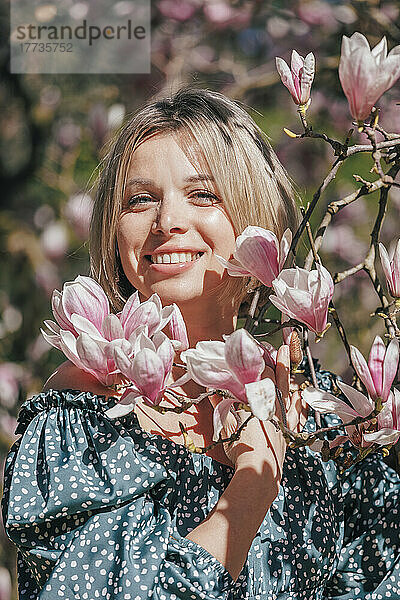 Lächelnde Frau  die an einem sonnigen Tag neben rosa Blumen steht