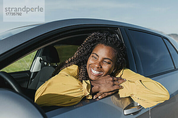 Glückliche Frau lehnt sich an einem sonnigen Tag aus dem Autofenster