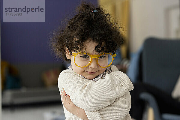 Cute little girl wearing oversized eyeglasses hugging self