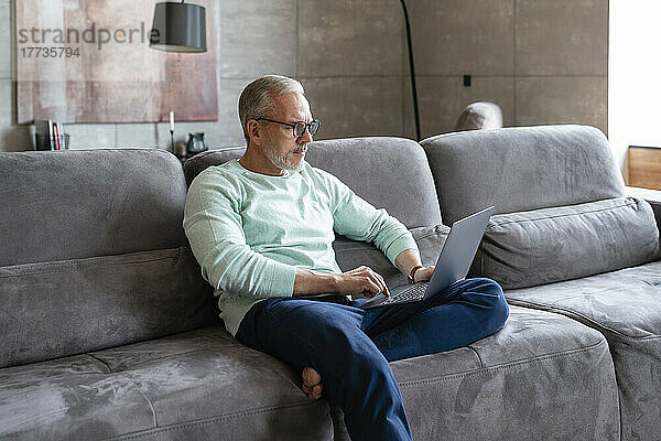 Geschäftsmann sitzt mit Laptop auf dem Sofa im heimischen Wohnzimmer