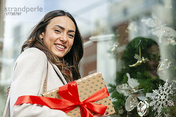 Glückliche Frau mit Weihnachtsgeschenk am Glasfenster