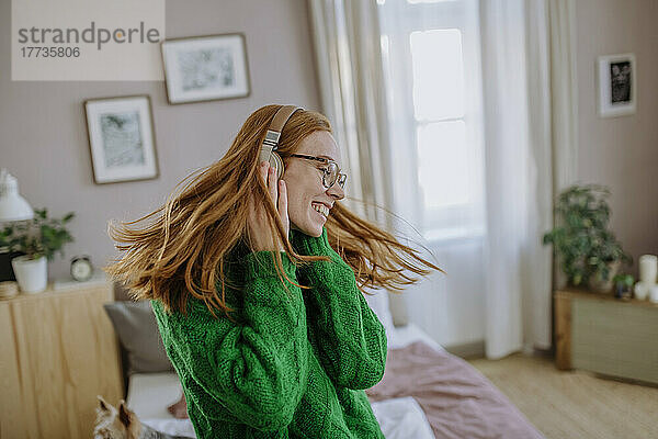 Glückliche Frau mit zerzausten Haaren  die zu Hause Musik über kabellose Kopfhörer hört