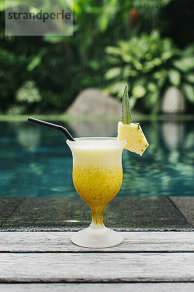 Pineapple cocktail standing on edge of swimming pool