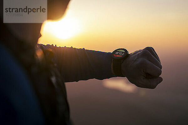 Mann überprüft Smartwatch bei Sonnenuntergang