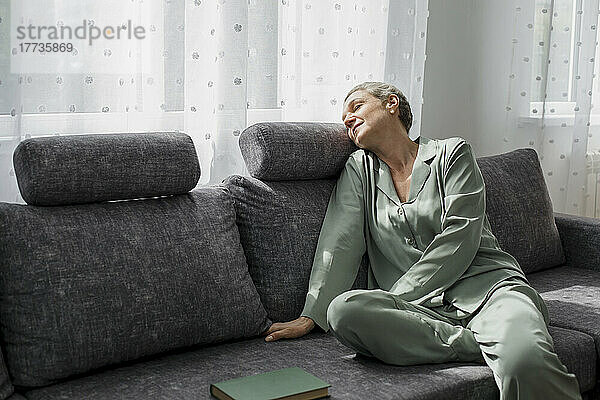 Entspannte reife Frau sitzt mit geschlossenen Augen auf der Couch im Wohnzimmer