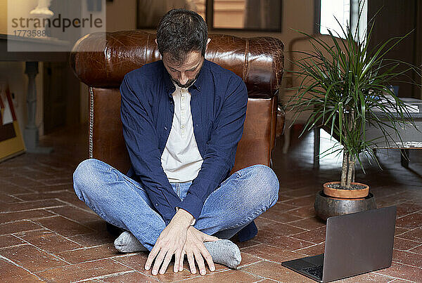 Mann sitzt zu Hause mit gekreuzten Beinen vor Laptop auf dem Boden
