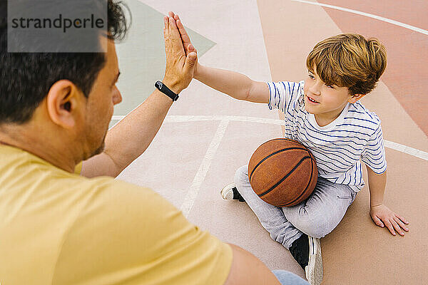 Junge mit Basketball gibt Mann auf Sportplatz High Five