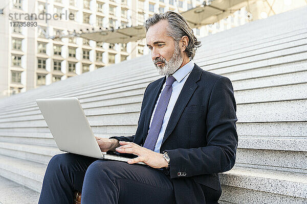 Reifer Geschäftsmann mit grauen Haaren sitzt mit Laptop auf Stufen
