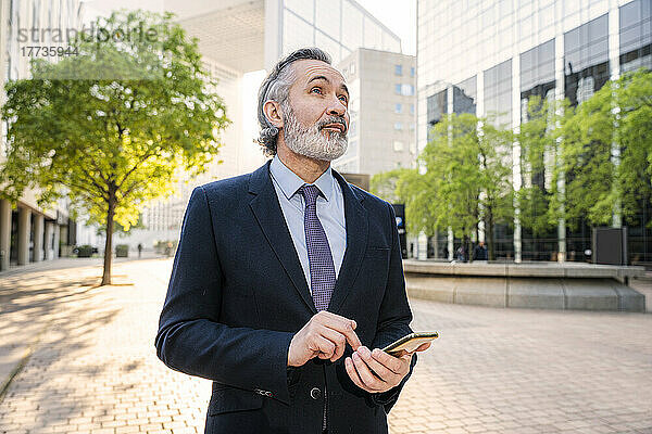 Reifer Geschäftsmann mit Mobiltelefon steht im Büropark