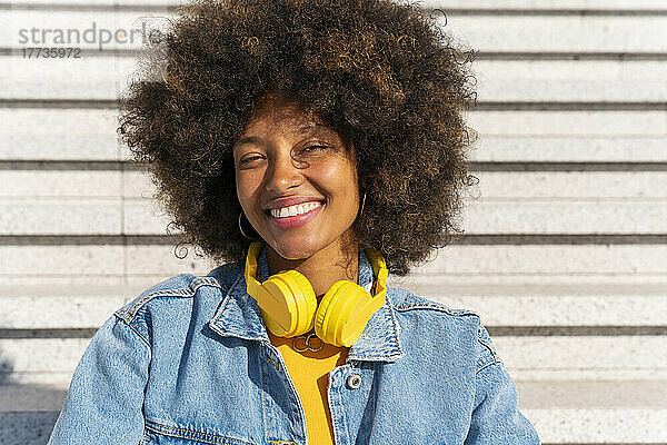 Glückliche schöne Afro-Frau mit kabellosen Kopfhörern auf Stufen