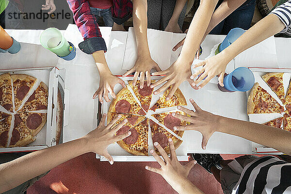 Hands of children reachuing for pizza on table