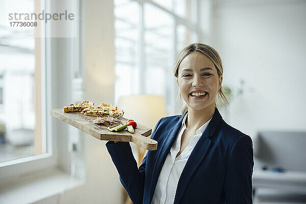 Lächelnde schöne Geschäftsfrau mit Sandwich auf Schneidebrett im Büro