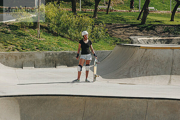 Frau trägt schützende Sportkleidung und hält Skateboard auf Rampe