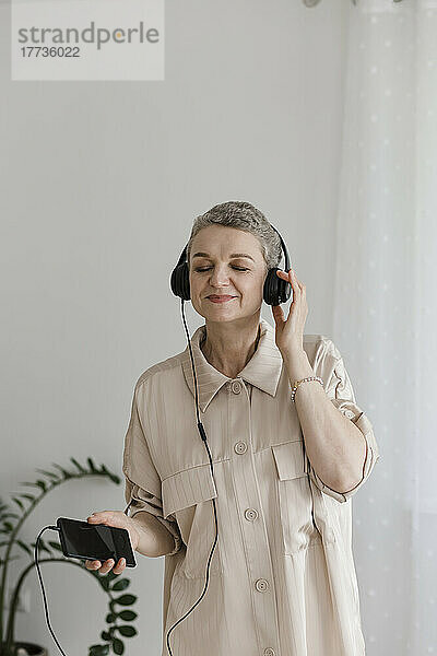Reife Frau trägt Kopfhörer und hört zu Hause Musik