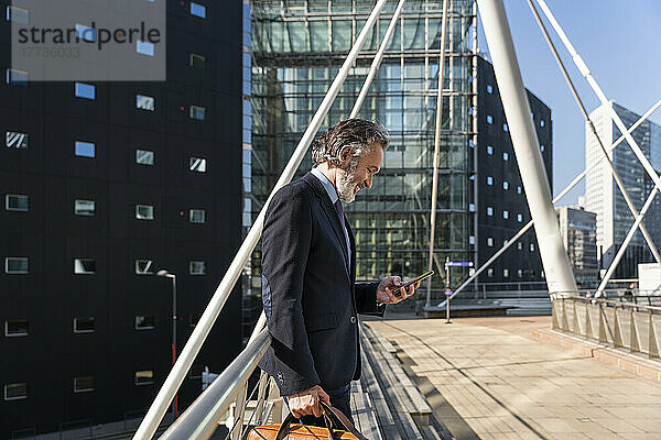 Glücklicher reifer Geschäftsmann  der sein Smartphone am Geländer benutzt