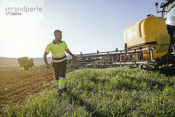 Farmer adjusting crop sprayer on field on sunny day
