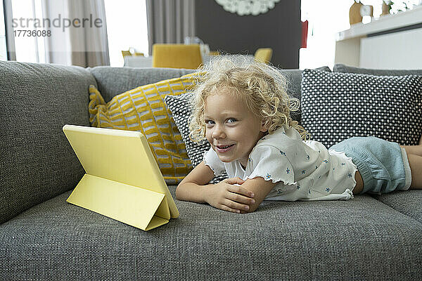 Lächelndes Mädchen  das zu Hause mit Tablet-PC auf dem Sofa liegt