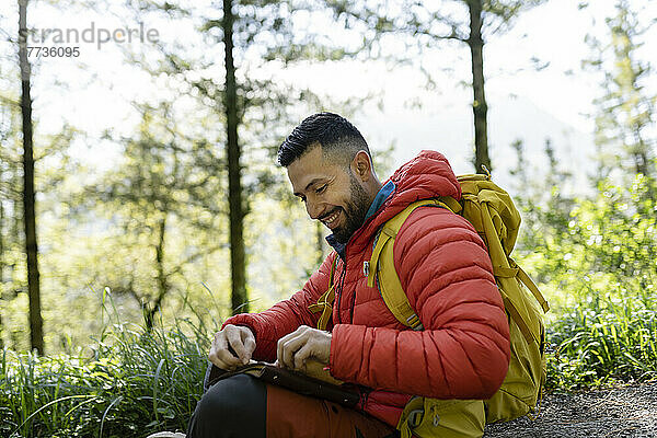 Glücklicher Mann mit Rucksack sitzt mit Tagebuch im Wald