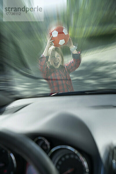 Verängstigter Junge mit Ball  der durch die Windschutzscheibe eines Autos gesehen wird und versucht  einen Unfall zu verhindern
