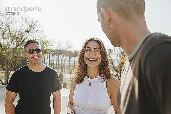 Glückliche Frau diskutiert an einem sonnigen Tag mit Männern im Skateboardpark