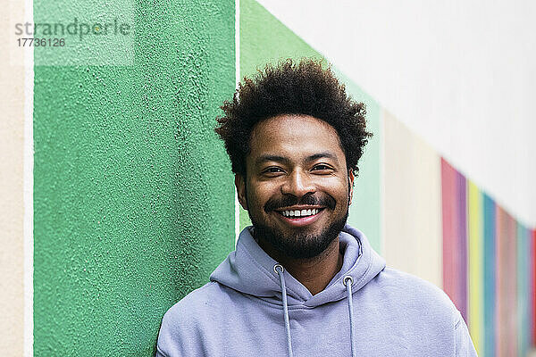 Lächelnder Afro-Mann lehnt an bunter Wand