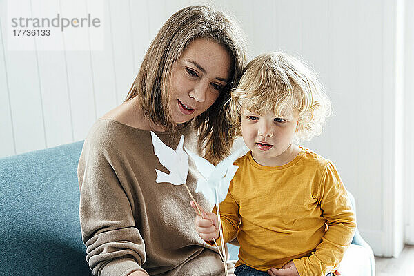 Mutter und Sohn halten Origami-Vögel in der Hand und sitzen zu Hause auf dem Sofa