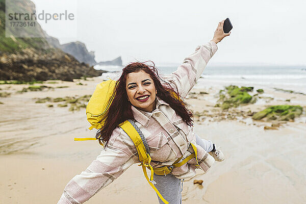 Lächelnde Frau hält Smartphone in der Hand und genießt den Strand