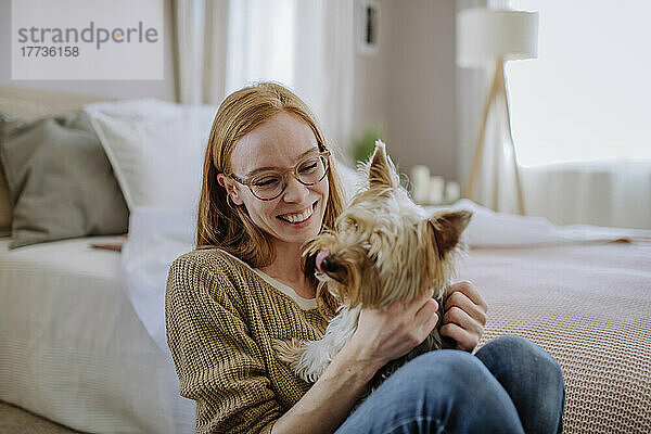 Fröhliche Frau mit Hund sitzt zu Hause am Bett