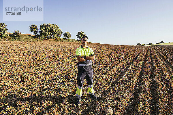 Bauer mit verschränkten Armen steht an einem sonnigen Tag auf dem Feld