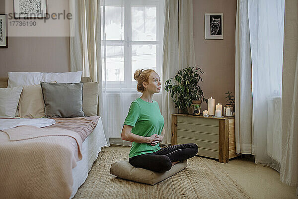 Frau sitzt mit gekreuzten Beinen und praktiziert zu Hause Yoga