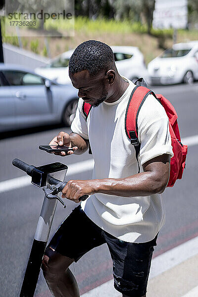 Junger Mann benutzt Smartphone und steht mit Elektroroller auf der Straße