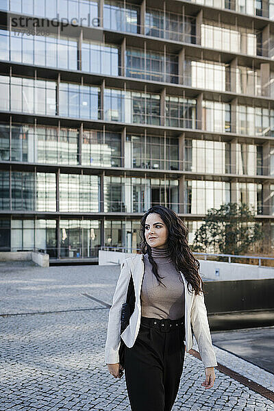 Junge Geschäftsfrau läuft vor einem modernen Bürogebäude