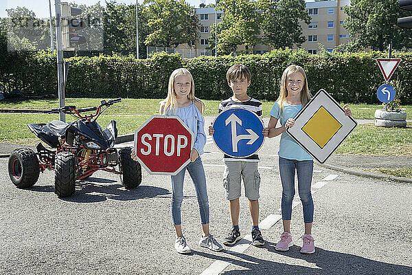 Lächelnde Kinder halten Verkehrsschilder auf stehender Straße