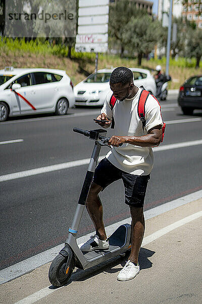 Junger Mann mit Elektroroller und Smartphone unterwegs