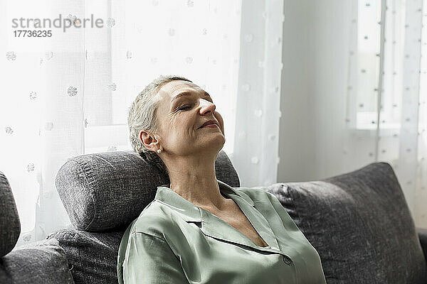 Relaxed mature woman on couch in living room with closed eyes