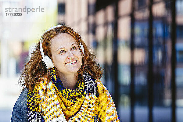 Glückliche Frau mit gelbem kariertem Schal  die über Kopfhörer Musik hört